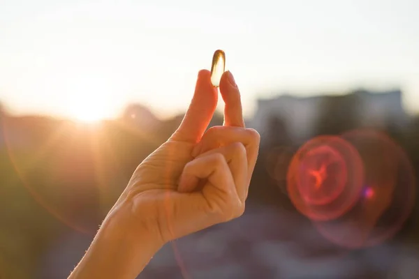 Aceite de pescado de mano Omega-3 cápsulas, fondo atardecer urbano . — Foto de Stock