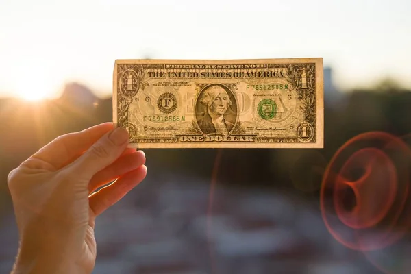 Mão segurando um dólar no fundo do sol . — Fotografia de Stock