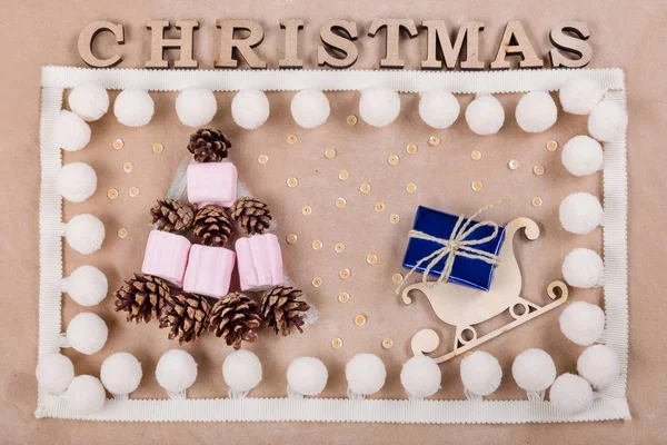 Sfondo natalizio con scatola regalo sulla slitta, coni e marshmallow sotto forma di albero di Natale. Kraft sfondo di carta, Vista dall'alto . — Foto Stock