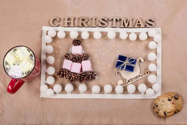 Sfondo natalizio con scatola regalo sulla slitta, tazza di caffè, biscotti, coni e marshmallow sotto forma di albero di Natale . — Foto Stock