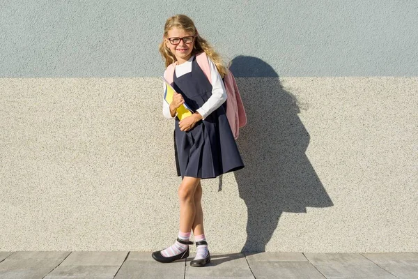 Chica en uniforme escolar, con una mochila, gafas y cuadernos. Fondo pared gris, Copiar spsce —  Fotos de Stock