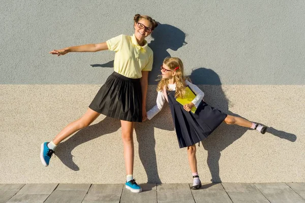 Две девочки школьницы начальной и старшей школы, позируя перед камерой, по пути в школу. Фоновая серая стена — стоковое фото