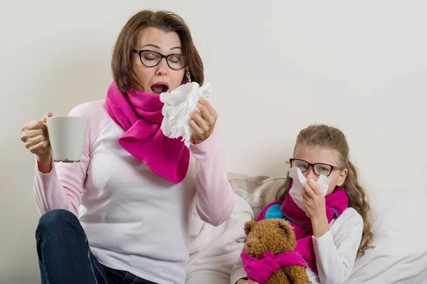 Madre e hija enfermas. Una mujer con secreción nasal, estornuda, usa un pañuelo, bebe té caliente, medicina . —  Fotos de Stock