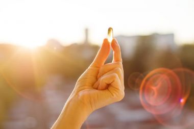 Balık yağı Omega 3 kapsülleri, kentsel günbatımı arka plan tutan bir kadın eli. Sağlıklı beslenme, tıp, sağlık, gıda takviyeleri ve insanlar kavramı