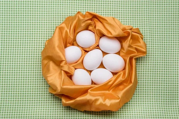Soyut bir yuvaya, mutfak masa örtüsü sarı dokular, yeşil arka plan beyaz yumurta. — Stok fotoğraf