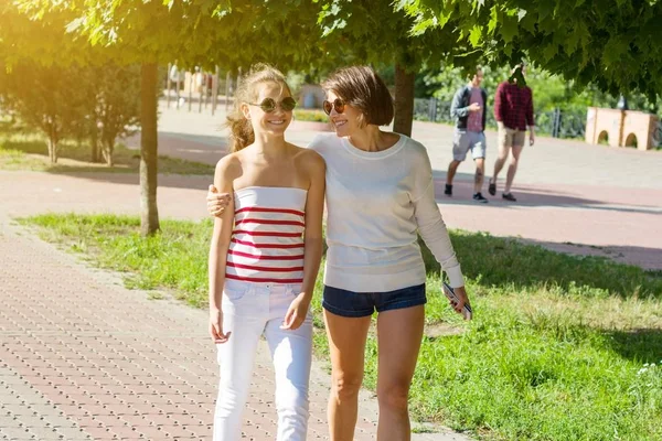 妈妈和女儿说话，笑着，穿过城市公园，在炎热的夏天 — 图库照片