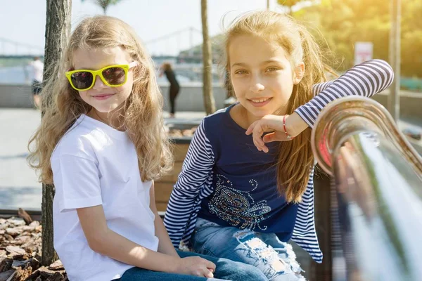 Dos niñas bonitas están mirando a la cámara y sonriendo. Fondo urbano, verano, terraplén del río —  Fotos de Stock