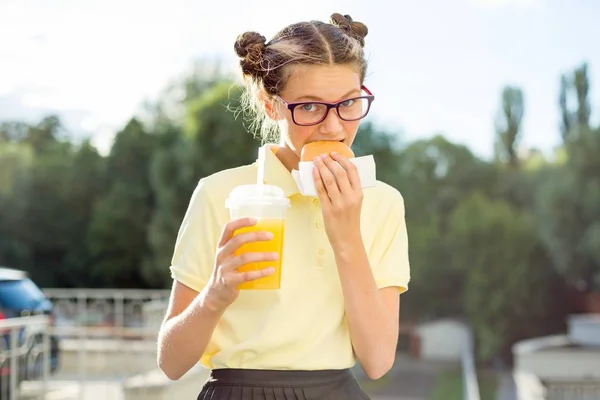 Adolescente bonito em uniforme escolar segurando um hambúrguer e suco de laranja. De volta à escola — Fotografia de Stock