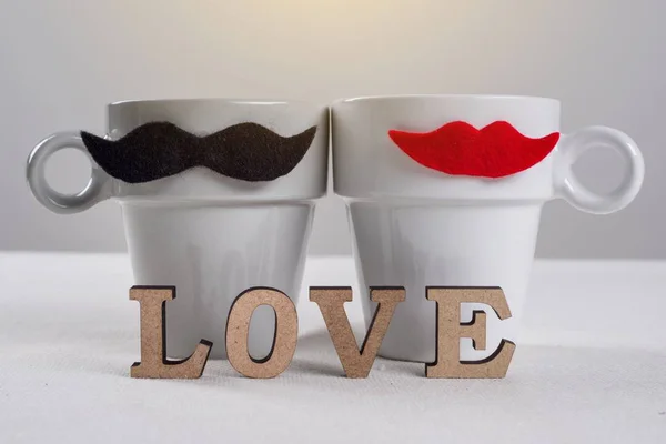 Fondo romántico del día de San Valentín. Un par de tazas de bigotes negros y labios rojos y una palabra de letras de madera - amor . — Foto de Stock