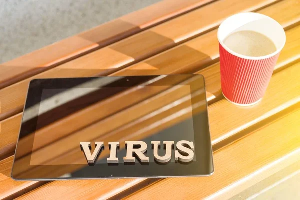 Word VIRUS with wooden vintage letters, background tablet on a wooden bench, cup of coffee — Stock Photo, Image