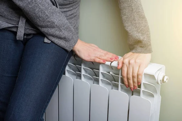La mujer está calentando sus manos en el panel del radiador —  Fotos de Stock