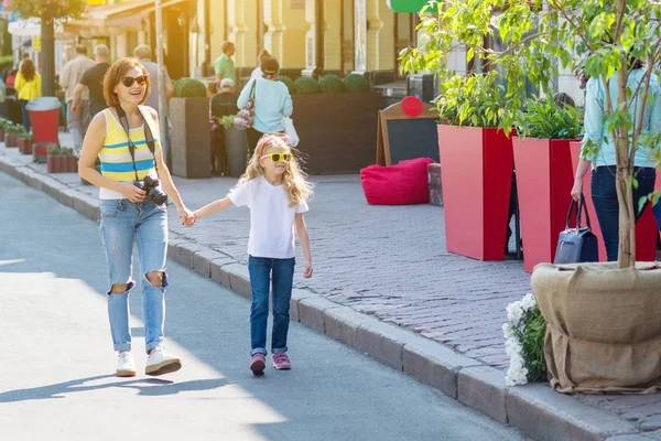 Mom and daughter holding hands walking around the city. Woman taking pictures at the camera, family tourism