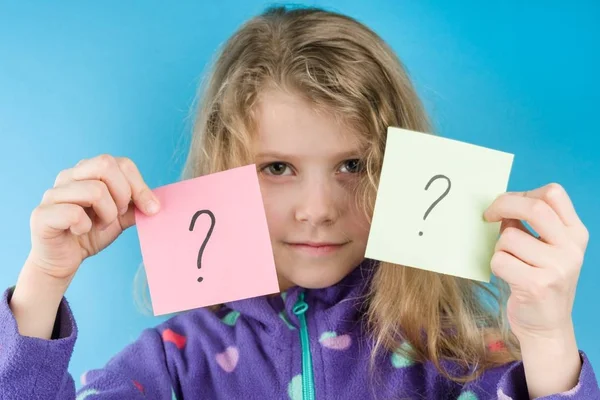 Chica sosteniendo pegatinas con signos de interrogación, fondo azul — Foto de Stock