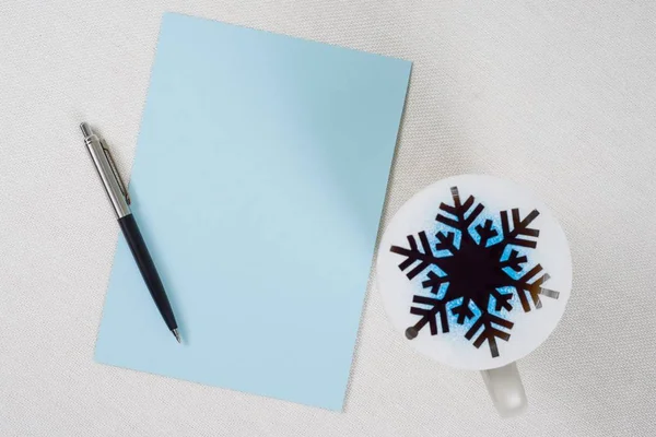 Foglio di carta blu puro su tavolo bianco. Penna, tazza di caffè e fiocco di neve astratto - simbolo dell'inverno, Natale — Foto Stock