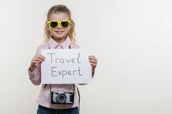 Girl child holding piece of paper with a word TRAVEL EXPERT. White bakgrounde, copy space — Stock Photo, Image