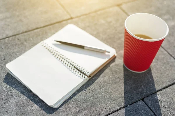 Open notebook with blank pages, pen and Cup of coffee on gray paving slab. Top view — Stock Photo, Image