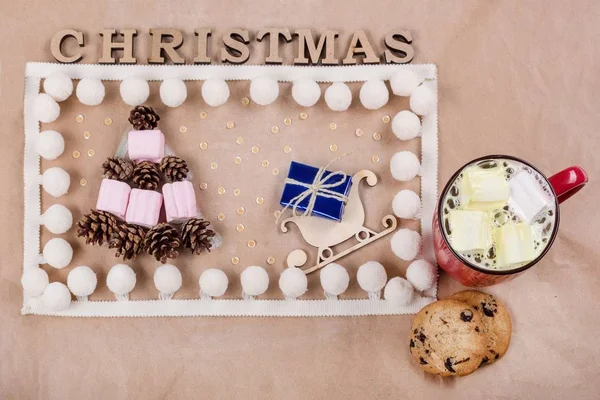 Sfondo natalizio con scatola regalo sulla slitta, tazza di caffè, biscotti, coni e marshmallow sotto forma di albero di Natale. Kraft sfondo di carta, Vista dall'alto . — Foto Stock