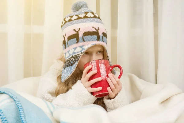 Het seizoen van de herfst winter. Meisje thuis in gebreide muts verpakt in tapijt, drinken van hete thee — Stockfoto