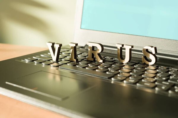 Word VIRUS with wooden vintage letters, a laptop keyboard background.