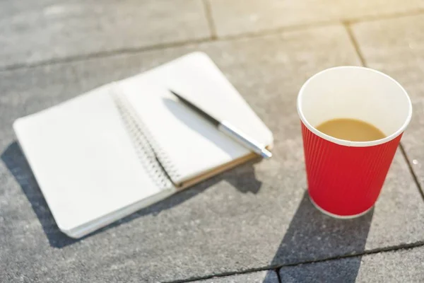 Abra o caderno com páginas em branco, caneta e xícara de café na laje de pavimentação cinza . — Fotografia de Stock