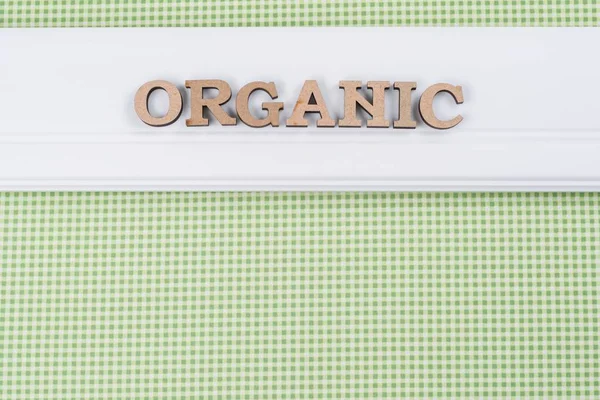 Palabra orgánica con letras abstractas de madera. Fondo panel blanco sobre una textura verde — Foto de Stock