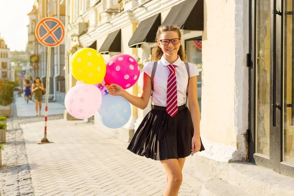 Meisje tiener middelbare scholier met ballonnen, op school uniform met bril gaat langs de straat stad. — Stockfoto