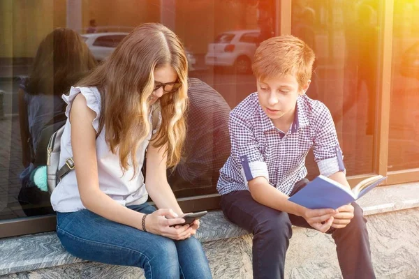 Niños adolescentes, leyendo libros y usando teléfonos inteligentes . — Foto de Stock