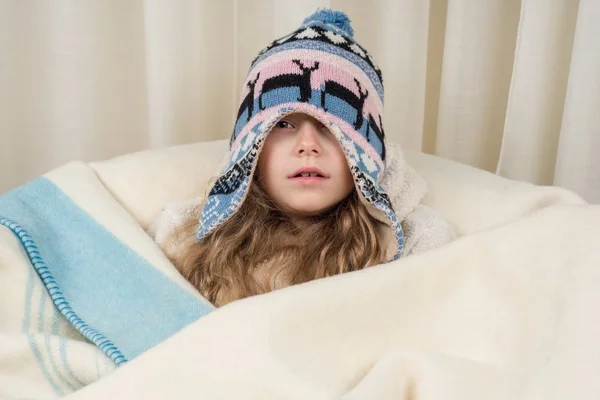 Η εποχή είναι Φθινόπωρο-Χειμώνας. Κορίτσι παιδί στο σπίτι σε ένα πλεκτό κάλυμμα τυλιγμένο σε καρό, συγκίνηση είναι κρύο — Φωτογραφία Αρχείου
