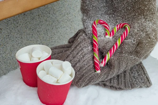 Twee kopjes koffie met marshmallow, twee kerst snoep stokken - hart, gebreide trui op de sneeuw bank — Stockfoto