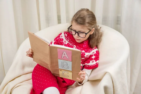 Niña en gafas aprende a leer un libro con el alfabeto . — Foto de Stock