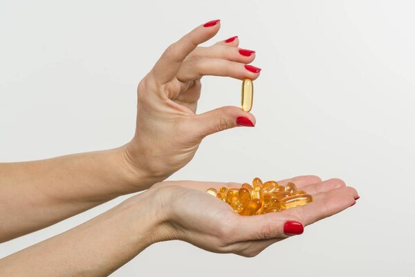 Hand holding capsule of Omega 3, white background