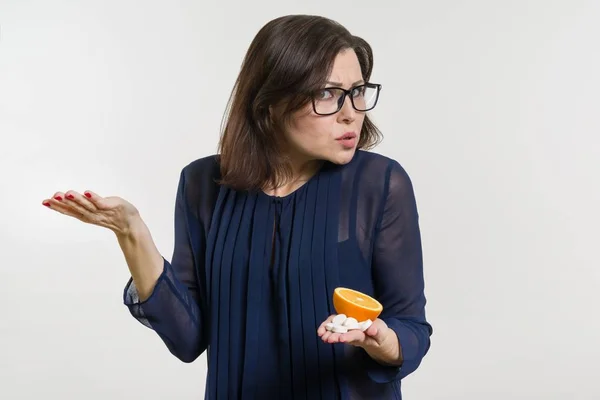 Woman holds a natural vitamin-orange in one hand and a synthetic vitamin C in the other. Makes a choice — Stock Photo, Image