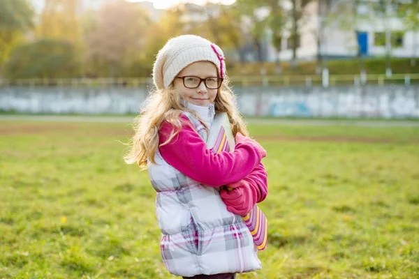 Portret van schattige aucasian meisje 7 jaar oud, met blond lang krullend haar, in glazen en een gebreide cap. — Stockfoto