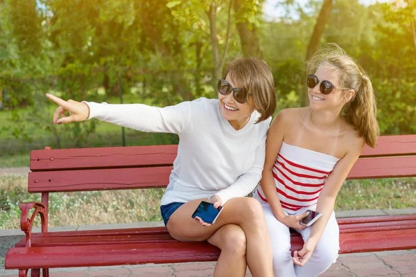 Mom and daughter teenager talking and laughing while sitting on the bench in the park — Stock Photo, Image