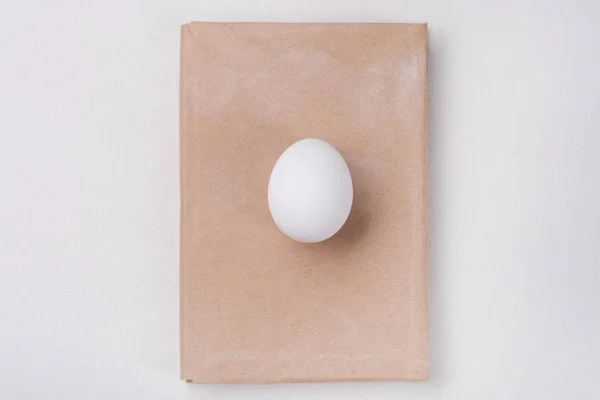 One white egg. Background - book in an old kraft cover. — Stock Photo, Image