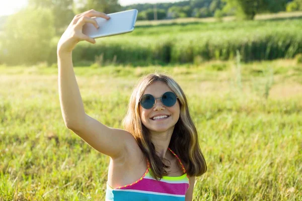 Fiatal tizenéves lány egy okostelefon, ezzel selfie a parkban. — Stock Fotó