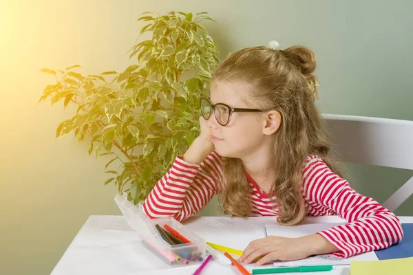 La colegiala joven de 7 años se sienta a la mesa y escribe la tarea escolar — Foto de Stock