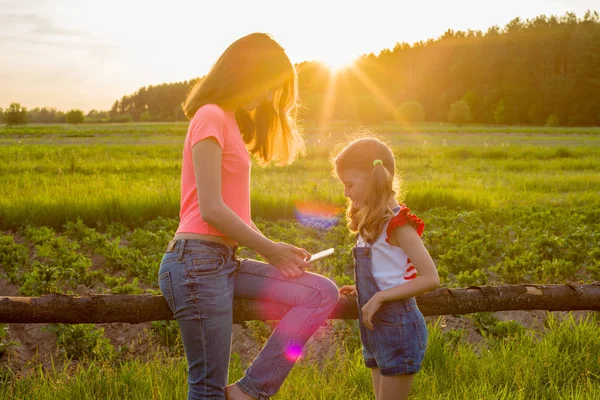 Hildren en el fondo de la naturaleza jugar con un teléfono inteligente . — Foto de Stock