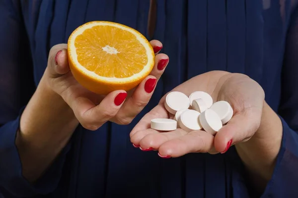 Eine Frau hält in der einen Hand eine natürliche Vitamin-Orange und in der anderen ein synthetisches Vitamin C. — Stockfoto