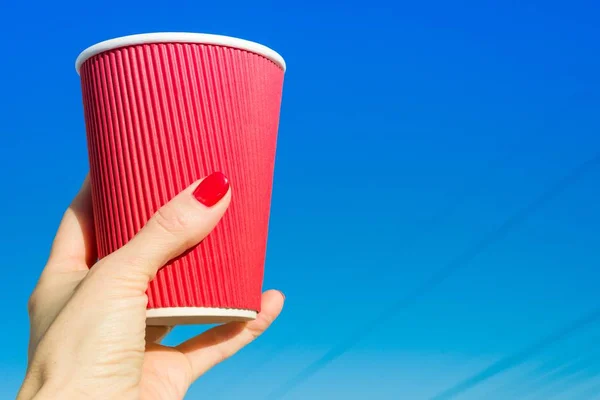 Red paper glass in female hand, background blue clear sky — Stock Photo, Image