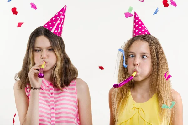 Filles sur un fond blanc, en chapeaux de fête, soufflant dans les tuyaux, confettis colorés — Photo