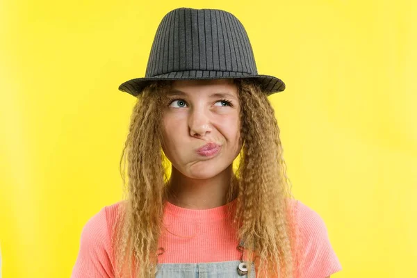 Menina bonita 12-13 anos loira com cabelo encaracolado em um chapéu, olha penosamente de lado, pensando sobre a escola . — Fotografia de Stock