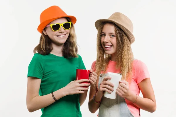 Flickvänner 12-14 år gammal, på vit bakgrund i hattar talar, håller koppar — Stockfoto