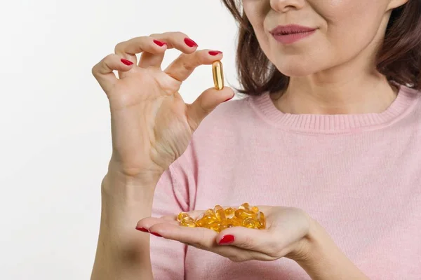 Una mujer sostiene una cápsula con vitamina E, aceite de pescado. fondo blanco, enfoque en la cápsula — Foto de Stock