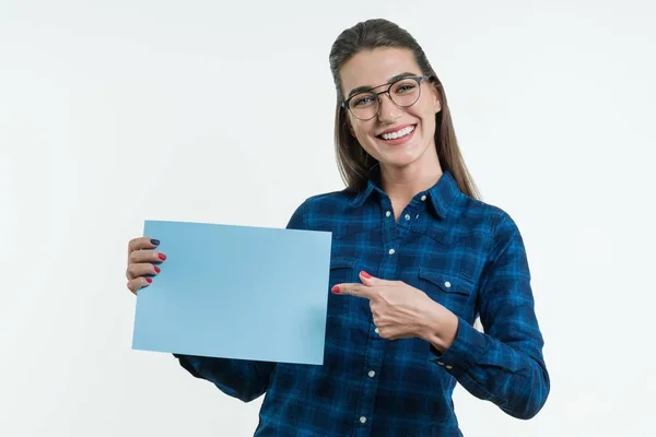 Estudante sorrindo positivo segurando uma folha limpa de papel azul, apontando um dedo para o papel . — Fotografia de Stock