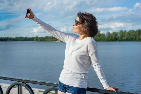 Uma mulher faz selfie usando um smartphone . — Fotografia de Stock
