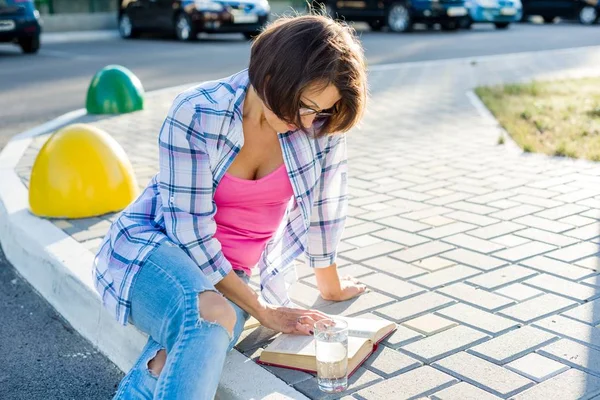 Улыбающаяся женщина пьет воду и читает книгу . — стоковое фото