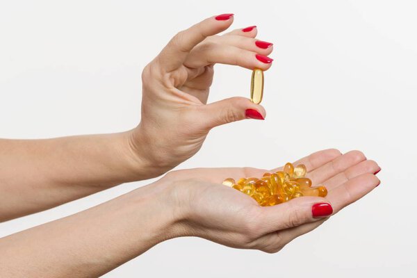 Hand holding capsule of Omega 3, white background
