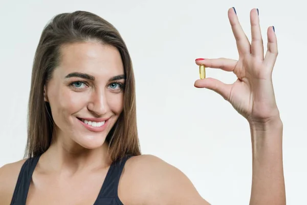 Frau hält eine Kapsel mit Vitamin E, Fischöl. weißer Hintergrund, Fokus auf die Kapsel — Stockfoto