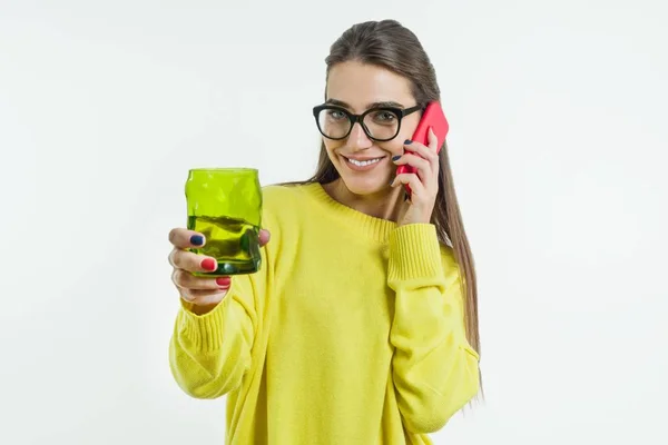 Retrato de uma jovem mulher sorridente bebendo água, suco de um copo verde, falando ao telefone, olhando para a câmera . — Fotografia de Stock